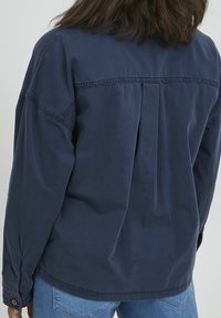 Navy blue long-sleeve shirt with a relaxed fit, buttoned cuffs, and a back pleat detail. Made of lightweight fabric with a smooth texture.