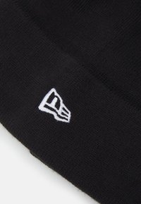 Berretto lavorato a maglia nero con logo ricamato bianco sul lato. Tessuto morbido con una vestibilità aderente, adatto per il freddo.