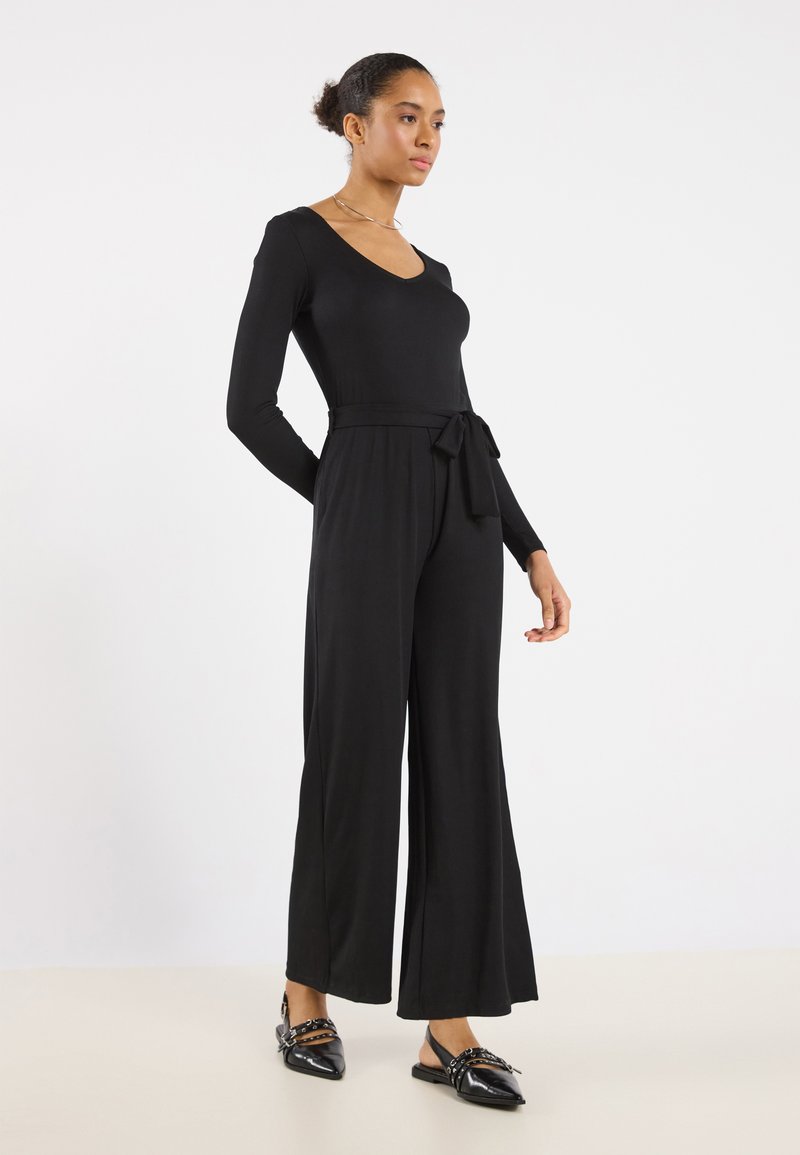 Black jumpsuit with long sleeves, V-neck, belted waist, and wide-leg trousers. Smooth texture with a fitted top, elegant design.