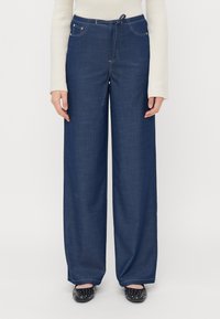 Bredde benbukser i mørk blå denim, med elastisk liv og snøring, frontlommer og kontrastsøm for ekstra detaljer.