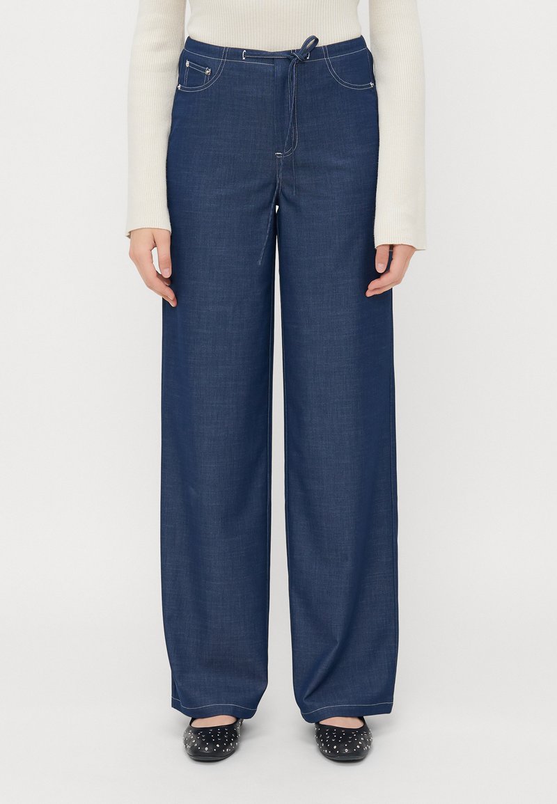 Bredde benbukser i mørk blå denim, med elastisk liv og snøring, frontlommer og kontrastsøm for ekstra detaljer.