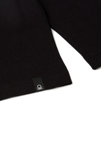 Czarna bawełniana koszulka z krótkim rękawem, z małą czarną metką z białym logo blisko dolnego brzegu, gładka tekstura.