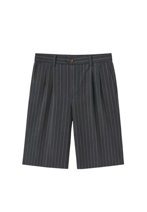 Osoba w ciemnoszarych, wąsko prążkowanych szortach do kolan, białych skarpetkach z czarnym napisem oraz beżowych zamszowych butach sznurowanych z grubymi podeszwami.