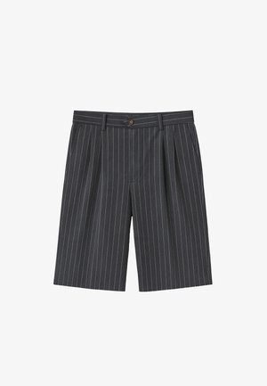 Persoon die donkergrijze, knielange shorts met krijtstrepen draagt, witte sokken met zwarte tekst en beige suède veterchoenen met dikke zolen.