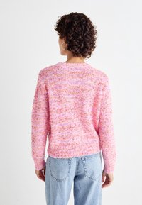 Růžový pletený svetr s texturovaným, vícero barevným vzorem. Kulatý výstřih a žebrované manžety, doplněný světle modrými džíny.