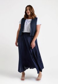 Falda larga de color azul marino fluida con pliegues, combinada con una camisa de manga corta blanca con bordado en azul, llevada debajo de un chaleco oscuro.