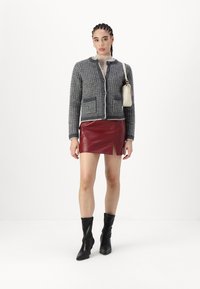 Pelēks teksturēts žakets ar divām priekšējām kabatām un kontrastējošu apdari, savienots ar pieguļošu sarkanu ādas svārku un melniem potīšu zābakiem. Mazs rokassomiņš.