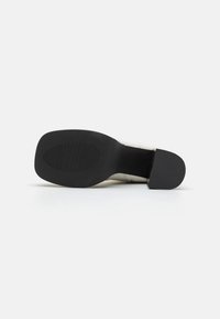 Zwarte rubberen zool met textuur voor grip, met een vierkante vorm en gladde randen. Het bovenste deel is crèmekleurig met subtiele stiksels.