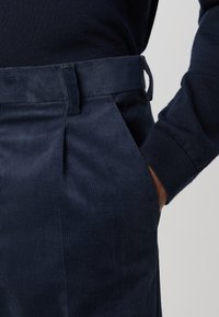 Marinblå vadmelbyxor med ränder, med midja som har bälteshällor, sidofickor och en slät textur.