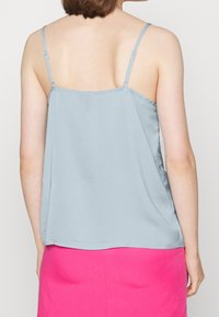 Ljusblå camisole med tunna justerbara band, slät textur och lös passform, i kombination med en starkt rosa kjol.