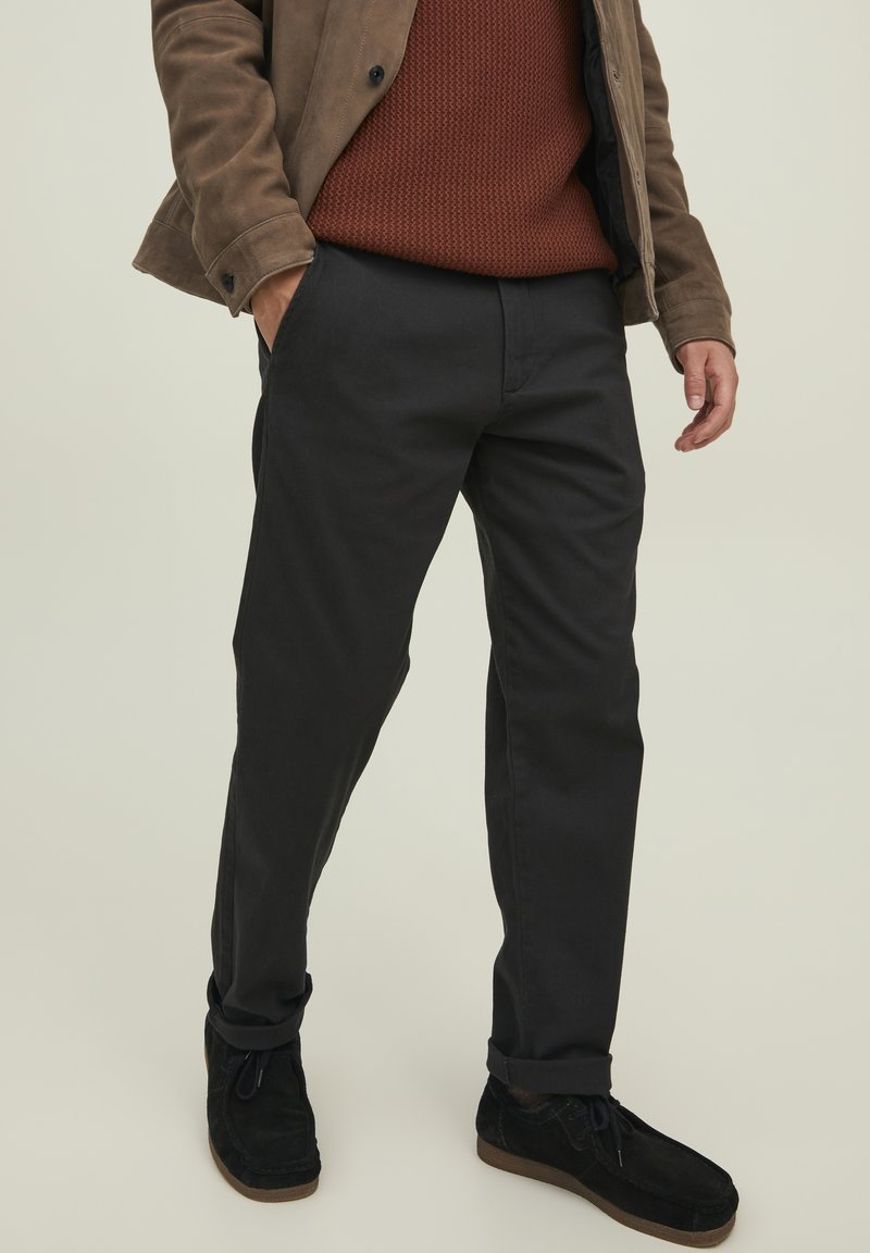 Pantalones de algodón negros de corte recto, con bolsillos laterales y una textura suave. Combinados con un suéter marrón de textura y zapatos oscuros.