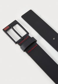 Curea din piele neagră cu un finisaj mat, având o cataramă rectangulară neagră și accente de cusătură roșie pe curea.