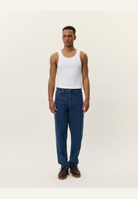 Mannen tanktop in het wit, gecombineerd met blauwe denim broek. De jeans hebben een relaxed fit en een klassiek vijf-pocket ontwerp. Bruine schoenen maken de look compleet.