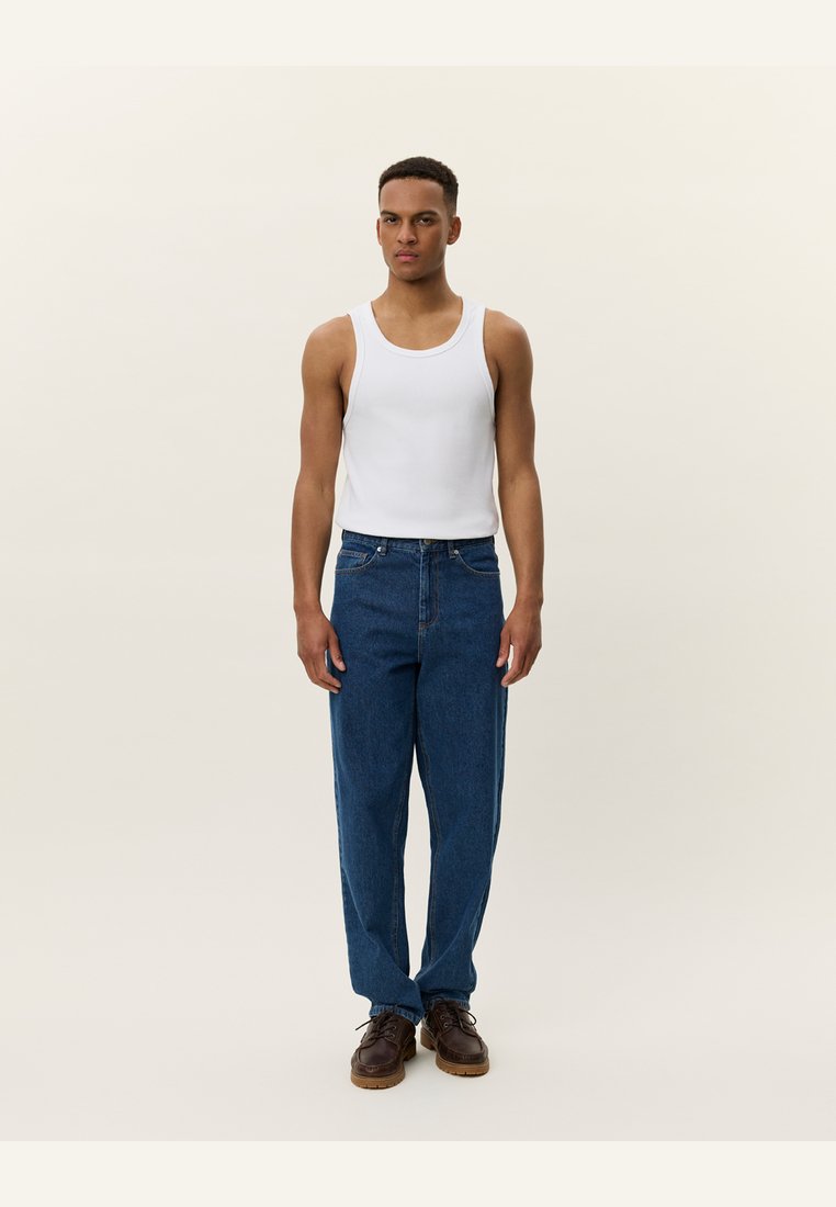 Mannen tanktop in het wit, gecombineerd met blauwe denim broek. De jeans hebben een relaxed fit en een klassiek vijf-pocket ontwerp. Bruine schoenen maken de look compleet.