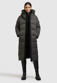Lungo cappotto imbottito grigio scuro con cappuccio, caratterizzato da trapuntature orizzontali e tasche laterali. Abbinato a stivali neri fino al ginocchio.