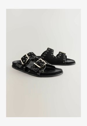 Mustad naha sandaalid, millel on kaks laia rihma koos suurte hõbedaste pandlite ja metallist silmadega, tekstureeritud jalanõusis ja tasane kummist talla.