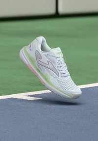 Scarpa sportiva bianca con una parte superiore testurizzata, caratterizzata da accenti lavanda e una suola verde chiaro. Presenta una forma arrotondata e dettagli in rete.