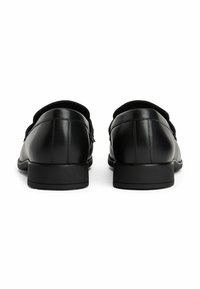 Un paio di scarpe eleganti in pelle nera viste da dietro, con tacco basso e impilato e cuciture sottili lungo le cuciture, su uno sfondo bianco.