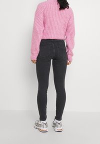 Jersey de punto rosa con cuello alto, combinado con jeans ajustados negros y zapatillas con detalles en plata, visto desde la parte de atrás.