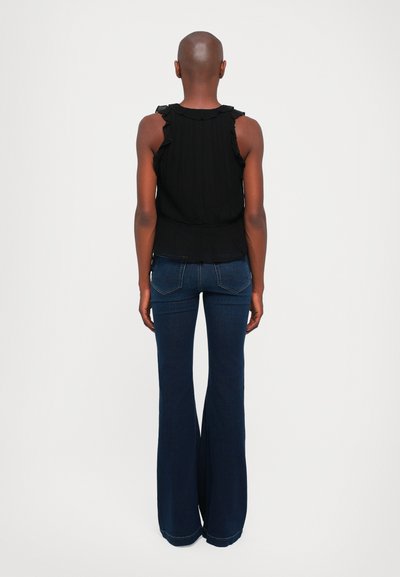 Zwarte mouwloze top met ruches, gecombineerd met uitlopende donkere denim jeans. De achterkant benadrukt de elastische taille en pasvorm van de top.