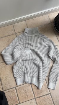 Gray ribbed knit sweater with a high neckline, long sleeves, and a relaxed fit. The fabric features vertical stripes and a soft texture.
