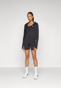 Svart atletisk bodysuit med korte ben, iført med en matchende svart hettejakke. Hvit Adidas-logo på brystet og skoene.