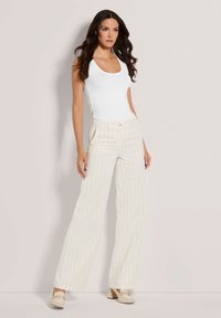 Witte tanktop gecombineerd met romige, wijde gestreepte broek met verticale lijnen; model draagt beige blockhak schoenen.