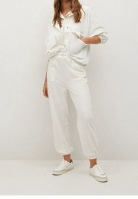 Witte oversized blouse met twee voorzakken, gecombineerd met elastische taille, tapered witte broek en witte sneakers; gladde stof en relaxte pasvorm.