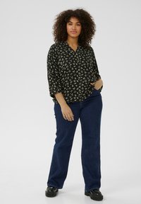 Blouse noire à motif floral avec une coupe décontractée et des manches trois-quarts, associée à un jean évasé bleu foncé et des chaussures à plateforme noires.