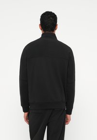 Μαύρη φούτερ μπλούζα με ψηλό γιακά, ραγλάν μανίκια και εμφανή ραφές. Διαθέτει μαλακό, υφασμάτινο υλικό και άνετη εφαρμογή.