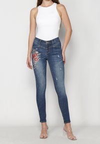 Tajta jeans i mörkblå denim med blommönster broderat på vänster lår, med fransar och en midjehög midja.