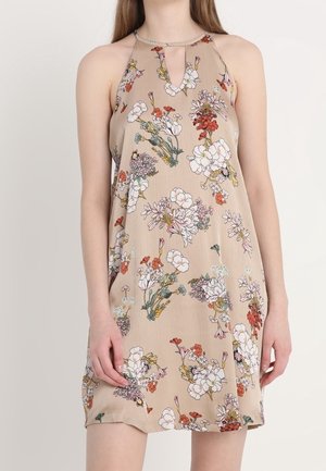 Sleeveless beige dress with halter neck and red, white, and yellow floral print worn by a standing person.