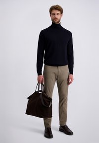 Czarny sweter z golfem, beżowe spodnie slim fit oraz ciemnobrązowa zamszowa torba z skórzanymi akcentami. Model stoi na jasnym tle.