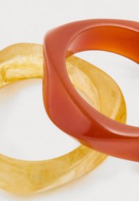 To bangles: en gjennomsiktig gul med en marmorert tekstur, og en glatt, buet rød bangle som overlapper den gule. Begge har avrundede kanter.