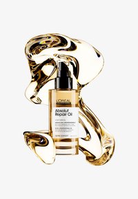 L'Oréal Absolut Repair Oil i en klar glassflaske med en svart pumpe. Olje svirrer rundt flasken, og viser en gyllen farge og jevn tekstur.
