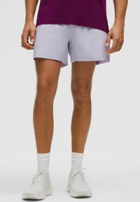 Ljuslila shorts med en slät yta, något ovanför knät, kombinerat med vita sportskor och vita ankelsockor.