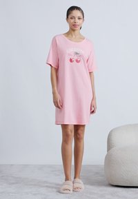 Ροζ βαμβακερό νυχτικό με κοντά μανίκια, με εκτυπωμένο σχέδιο κερασιών και κείμενο. Φοριέται με μπεζ αφράτες παντόφλες.