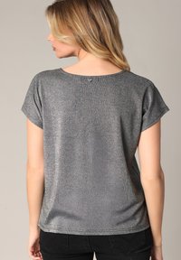 Top court à manches courtes en métal gris avec un col arrondi et un subtil effet chatoyant, présentant un petit détail de bouton à l'arrière.