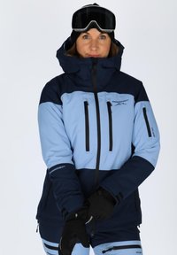 Ski jacket in light blue and navy with a hood, zippered pockets, and adjustable cuffs. Black gloves with logo details.