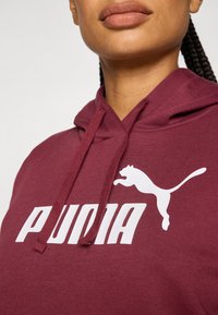Bordo dukserica s kapuljačom s bijelim logotipom "PUMA" i grafikom skakačkog mačka. Izrađena od mekog materijala s kapuljačom na vezanje.