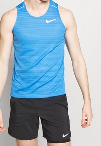 Blå atletisk tanktop med horisontale striber, lavet af letvægtsmateriale. Har et hvidt Nike-logo og rund udskæring, parret med sorte shorts.