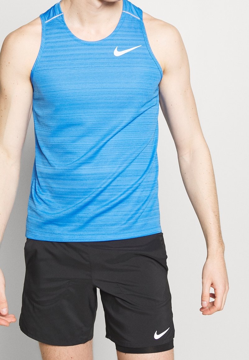 Blå atletisk tanktop med horisontale striber, lavet af letvægtsmateriale. Har et hvidt Nike-logo og rund udskæring, parret med sorte shorts.