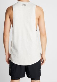 Top deportivo sin mangas de color blanco con una tela texturizada, escote redondo y logotipo en la parte de atrás, combinado con pantalones cortos deportivos negros.