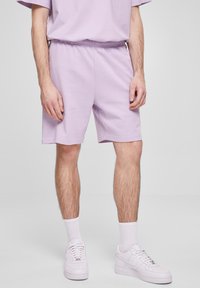 Lilla bomullsshorts med elastisk midje, avslappet passform og sidelommer, kombinert med hvite joggesko og sokker.