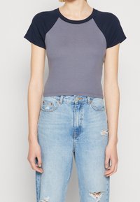 Šedý crop top s námořnickými raglánovými rukávy, vyrobený z měkké látky. Kombinovaný s vysokým pasem ležérními světle modrými džínami s outfitem s roztrhanými akcenty.