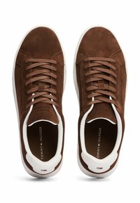 Sneakers in suede marrone con suole in gomma bianca, dotati di lacci piatti e punta tonda. Il logo del marchio è visibile sulla soletta e sulla linguetta della scarpa.