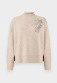 Maglione beige chiaro realizzato in morbido tessuto, con un collo alto e intricate decorazioni argentate sul lato sinistro. Polsini e orlo a costine.