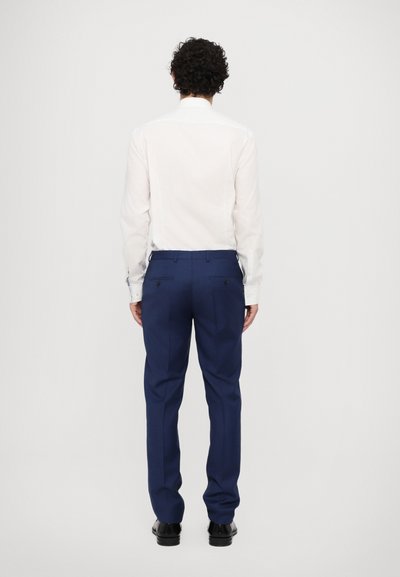 Chemise blanche à manches longues assortie à un pantalon bleu marine. La chemise est dotée d'un col standard, tandis que le pantalon présente des poches arrière et une coupe ajustée.