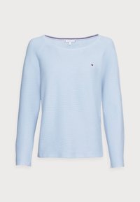 Pull bleu clair à manches longues avec un col large, une texture côtelée et un petit logo sur le côté gauche de la poitrine. Matière douce.