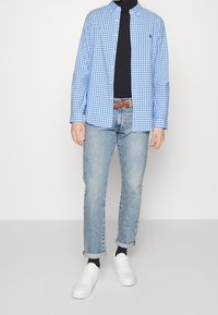 Blå och vit rutig skjorta med knappar, svart polotröja, ljusblå upprullade jeans, brun flätad bälte och vita sneakers.